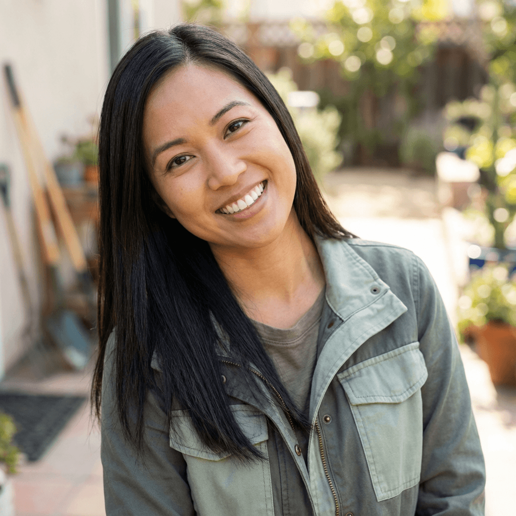 Portrait of a happy female homeowner, Emily Rodriguez, standing in a sunny front yard with a green lawn.